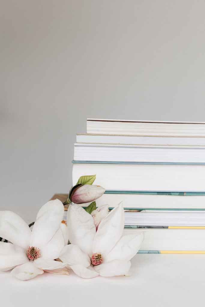 stack of books near blooming magnolia flowers