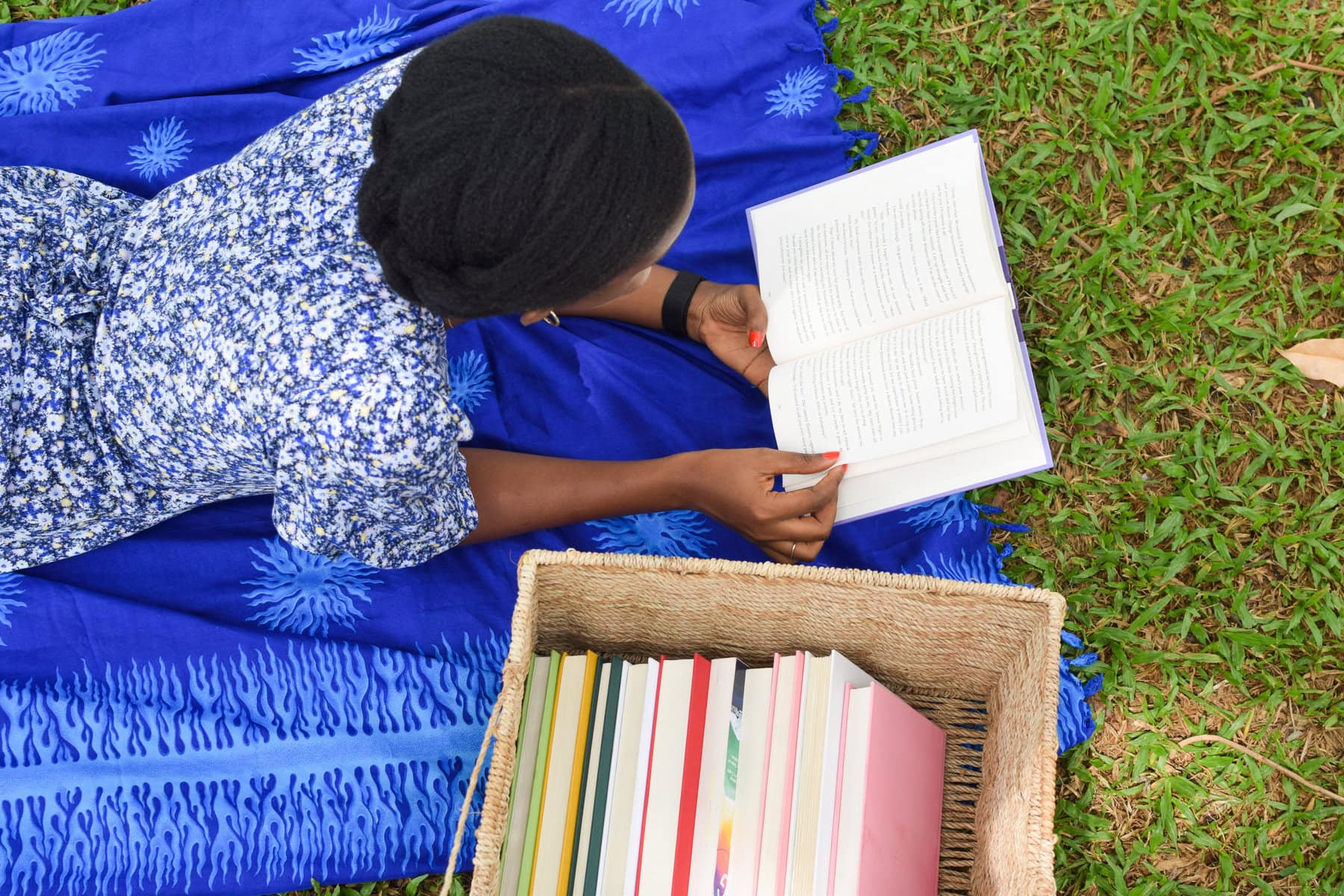 afoma lays on grass with an open book and a basket of books nearby